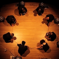 people in a circle holding a rope with laptops and speakers next to them